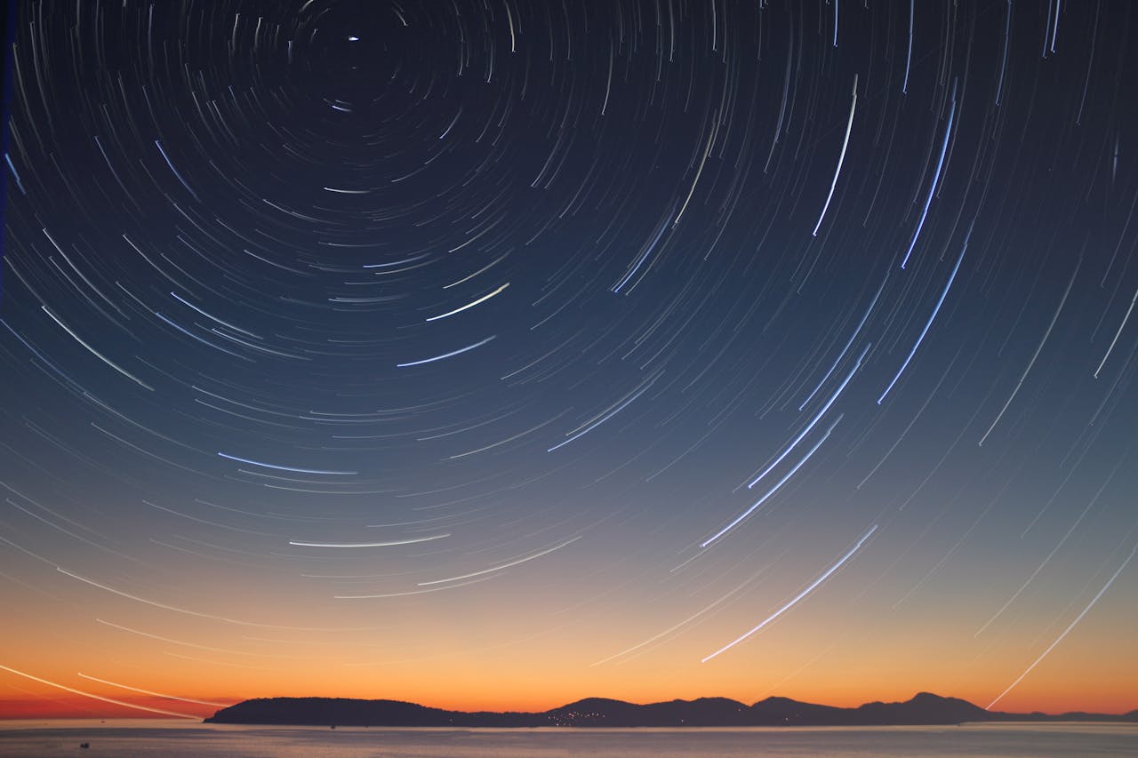A stunning long exposure of star trails over the ocean horizon at twilight.